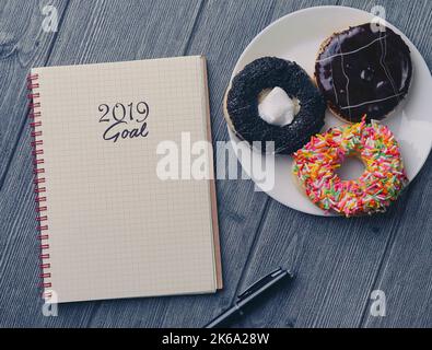 Draufsicht auf Notizbuch, Kugelschreiber und Donut auf Holzhintergrund mit 2019 Tor Stockfoto