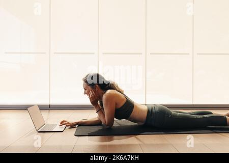 Fröhliche ältere Frau, die lächelt, während sie an einem Online-Yoga-Kurs auf einem Laptop teilnehmen. Frau nach einem virtuellen Fitness-Tutorial zu Hause. Fröhliche reife Frau l Stockfoto