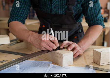 Ein Zimmermann mißt Holzbohlen und macht in einer Werkstatt mit einem Bleistift Markierungen. Stockfoto