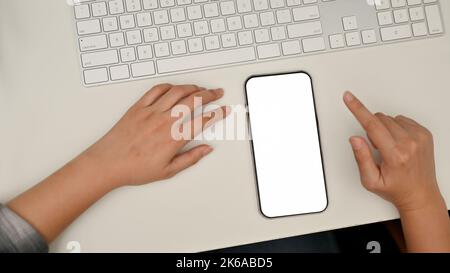 Eine Frau sitzt an ihrem Schreibtisch, Smartphone-Modell mit weißem Bildschirm und Tastatur auf einem weißen Tisch Stockfoto