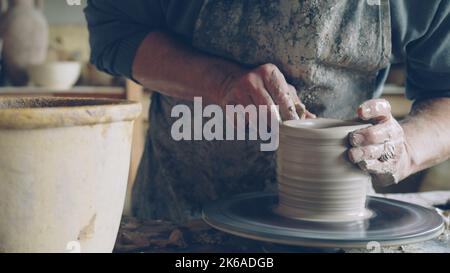 Close-up shot of half-finished ceramic vase spinning on potters's wheel and male hands molding clay with professional tools. Creating eathenware and traditional pottery concept. Stockfoto