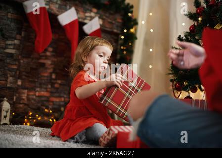 Geschenke machen. Kleines Mädchen mit Weihnachtsgeschenken. Frohe Weihnachtszeit für die Familie am Kamin Stockfoto