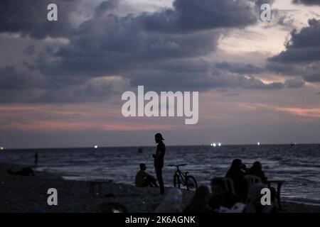 Gaza, Palästina. 12. Oktober 2022. Palästinenser sitzen während des Sonnenuntergangs westlich des zentralen Gazastreifens am Ufer des Mittelmeers. Kredit: SOPA Images Limited/Alamy Live Nachrichten Stockfoto