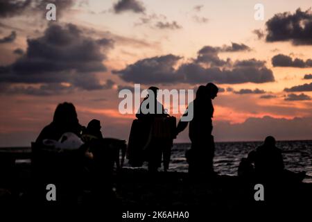 Gaza, Palästina. 12. Oktober 2022. Palästinenser sitzen während des Sonnenuntergangs westlich des zentralen Gazastreifens am Ufer des Mittelmeers. (Foto von Mahmoud Issa/SOPA Images/Sipa USA) Quelle: SIPA USA/Alamy Live News Stockfoto