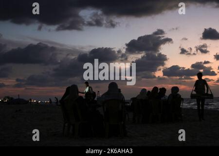 Gaza, Palästina. 12. Oktober 2022. Palästinenser sitzen während des Sonnenuntergangs westlich des zentralen Gazastreifens am Ufer des Mittelmeers. (Foto von Mahmoud Issa/SOPA Images/Sipa USA) Quelle: SIPA USA/Alamy Live News Stockfoto