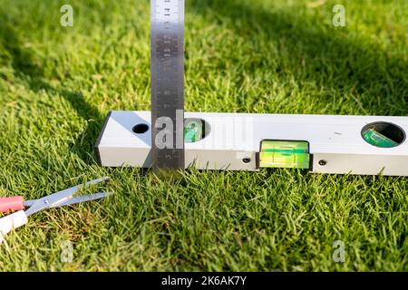 Messen des Grases mit Lineal und Nivellieren mit einem Wasserwaage-Werkzeug nach dem Schneiden des Grases. Complusive Obsessive Disorder Stockfoto