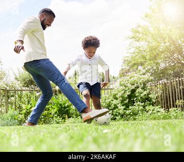 Der beste Weg, um Spaß in der Sonne zu haben. Ein Vater und ein Sohn spielen gemeinsam Fußball im Freien. Stockfoto