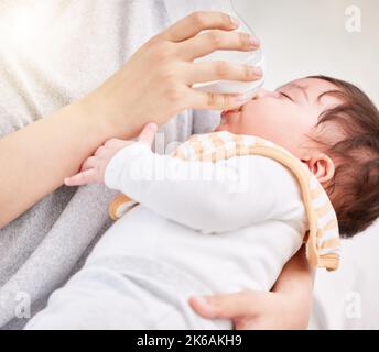 Nahaufnahme eines niedlichen müden kleinen neugeborenen Brünette gemischtes Rennen Baby, das von unbekannter alleinerziehender Mutter in der Flasche gefüttert wird. Hispanische Baby nimmt sein Routine-Nickerchen Stockfoto