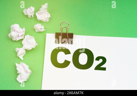 Ökologisches Konzept. Auf grünem Hintergrund zerknittertes Papier und ein Blatt mit der Aufschrift - CO2 Stockfoto