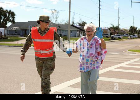 Port Charlotte, Florida, USA. 2. Oktober 2022. Avenger Crew Member Spc. Elizabeth Strople, 1-256. Air Defense Artillery (ADA), unterstützt Susan Williams bei der Durchquerung einer stark frequentierten Kreuzung, während sie die Verkehrskontrolle für Zivilisten und Rettungskräfte in Port Charlotte, Flac, durchführte.über 6.000 Dienstmitglieder wurden als Reaktion auf die Naturkatastrophe aktiviert, zusammen mit militärischer und ziviler Unterstützung von Orten außerhalb des Bundesstaates. Kredit: U.S. Army/ZUMA Press Wire Service/ZUMAPRESS.com/Alamy Live Nachrichten Stockfoto