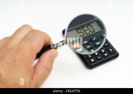 Geschäfts- und Finanzkonzept. Ein Mann schaut durch eine Lupe auf einen Rechner auf dem Bildschirm, von dem es geschrieben ist - SEO Stockfoto