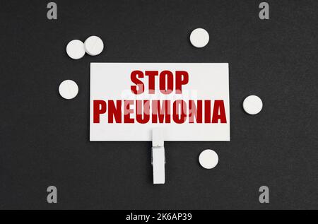 Medizinkonzept. Auf schwarzem Hintergrund befinden sich Pillen und eine Visitenkarte mit der Aufschrift - STOP PNEUMONIA Stockfoto