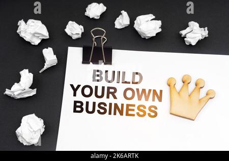 Geschäfts- und Finanzkonzept. Auf schwarzem Hintergrund, zerknittertes Papier und ein Blatt mit der Aufschrift - Build Your Own Business Stockfoto