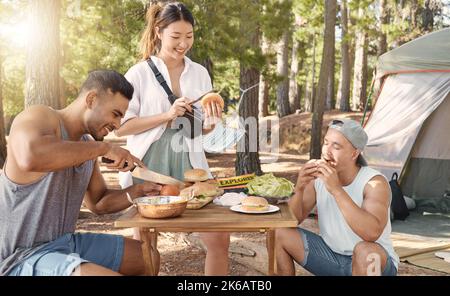 In der Natur zu sein macht hungrig. Eine vielfältige Gruppe von Freunden genießt ein gemeinsames Essen während eines Tages im Wald. Stockfoto