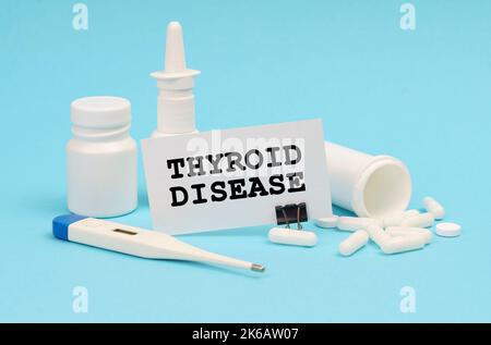 Medizinkonzept. Auf blauem Hintergrund ein Thermometer, Pillen und eine Visitenkarte mit der Aufschrift - SCHILDDRÜSENERKRANKUNG Stockfoto