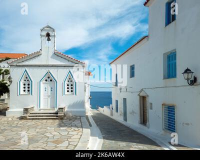 Agia Varvara Kirche auf Andros Insel Kykladen Griechenland. Weiß getünchten Tempel mit Dreieck-Fenster Tür, Glockenturm gepflasterten Hof in Chora. Meer, Himmel Hintergrund. Stockfoto