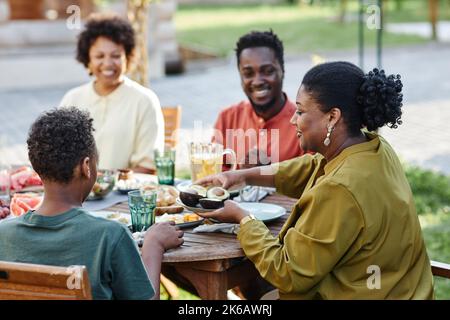 Seitenansicht Porträt einer jungen schwarzen Frau, die der Familie gesundes Essen serviert, während sie gemeinsam im Freien zu Abend gegessen hat Stockfoto