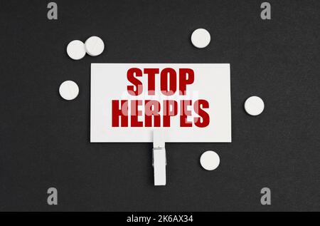 Medizinkonzept. Auf schwarzem Hintergrund befinden sich Pillen und eine Visitenkarte mit der Aufschrift - STOP HERPES Stockfoto