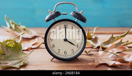 Sommerzeit, Fall Back. Schwarzer Wecker und Herbstblätter auf Holztisch Stockfoto