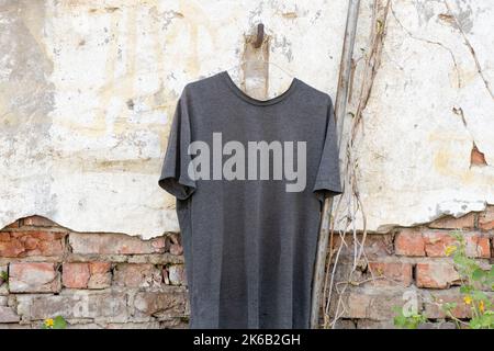 Graues T-Shirt an Kleiderbügeln, die in der Sonne auf der Straße an der Wand hängen, Mode und Trends, Kleidung Stockfoto