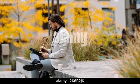 Ein ernsthafter Geschäftsmann in formeller Kleidung, der auf der Straße in der Stadt arbeitet Stockfoto