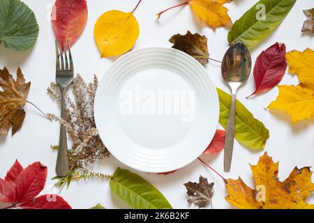 Essteller steht im Herbst auf einem weißen Tisch gelb-rote Blätter, Tischdekor im Herbst, Besteck, Tischdekorationen, Herbstsaison, Tabelleneinstellung Stockfoto