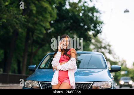 Frau telefoniert in der Nähe des Autos auf der Straße Stockfoto