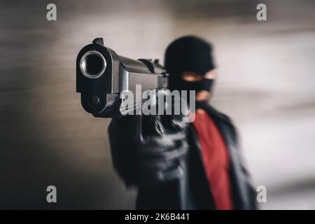 shooter in schwarzer Maske Angriffe. Bewaffneter Terrorist, Dieb mit Pistole in den Händen. Kriminelle zielen mit Waffe. Mafia Gangster Point gun in der Kamera. Konzentrieren Sie sich auf Stockfoto