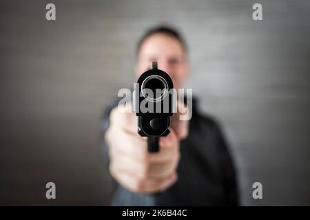 Brutaler, wütender Gangmannstil. Gangster in Aktion, Killer mit Pistolenpistole. Guy schießen Feuerwaffe Handfeuerwaffe, Pistole in einem Schießstand Stockfoto
