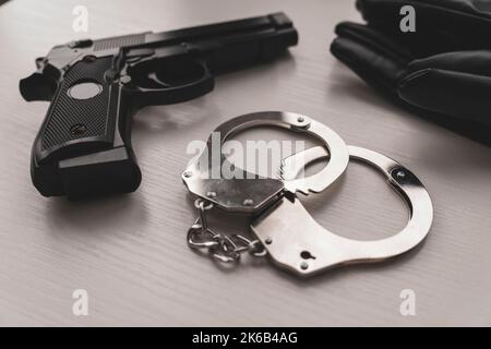 Pistole und Handschellen auf weißem Tisch. Munitionierung von Strafverfolgungsbehörden. Schusswaffen für die Polizei. Arrest-Konzept. Stockfoto