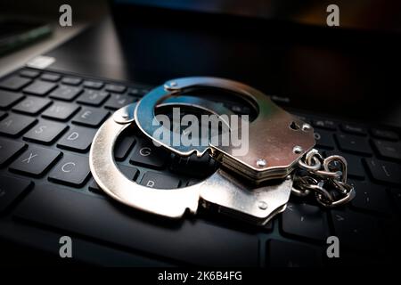 Computertastatur und Handschellen. Konzept für Cyberkriminalität, Internetsicherheit und Kriminalität. Metallhandschellen auf einer schwarzen Tastatur. Stockfoto