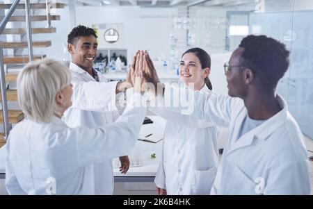 Eine vielfältige Gruppe glücklicher Wissenschaftler, die sich gegenseitig ein hohes Give geben, um ihren Erfolg zu feiern, während sie in einem Labor bei der Arbeit stehen. Team von vereinten Arbeitern Stockfoto