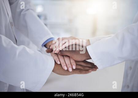 Verschiedene Ärztegruppen stehen mit gestapelten Händen, um sich gegenseitig zu motivieren. Gruppe von medizinischen Fachkräften zusammenarbeiten, jubeln zusammen in einem Stockfoto
