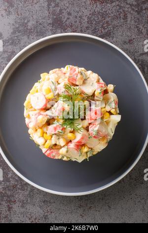 Einfacher Salat mit Krabbenstäbchen, Eiern, Zwiebeln und Mais mit Mayonnaise aus der Nähe auf einem Teller auf dem Tisch. Vertikale Ansicht von oben Stockfoto
