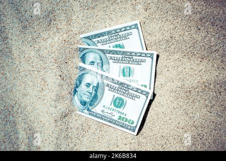 Gelddolare, die halb mit Sand bedeckt sind, liegen in der Nähe des Strandes. Dollarscheine teilweise im Sand vergraben. Dreihundert Dollar im Sand am Meer Ozean Strand begraben Konzept finanzieren Geld Urlaub entspannen Urlaub Stockfoto