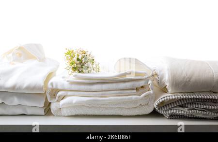 Sauberes weißes, frisch gewaschene und gefaltete Bett und kleiden Sie Ihre Kleidung auf einem weißen Tisch und einem isolierten Hintergrund. Vorderansicht. Horizontale Zusammensetzung. Stockfoto