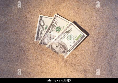 Gelddolare, die halb mit Sand bedeckt sind, liegen in der Nähe des Strandes. Dreihundert Dollar im Sand auf Meer oder Meer Strand begraben Konzept finanzieren Geld Urlaub entspannen Urlaub. Sonniger Sommer warmer Windtag. Stockfoto