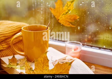 tasse Tee, Bücher, Herbstblätter und Kerze auf der Fensterbank zu Hause Stockfoto