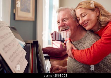 Lächelndes Senior-Paar Zu Hause, Das Gerne Klavier Spielt Stockfoto