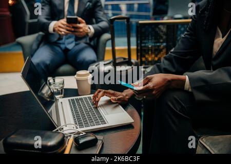 Mittelteil einer Geschäftsfrau, die in der Lounge des Hotels mit einem Laptop die Kreditkarte hält Stockfoto