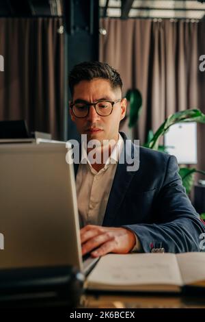 Ein mittelerwachsener Geschäftsmann, der in der Lounge des Hotels eine Brille trägt und einen Laptop benutzt Stockfoto