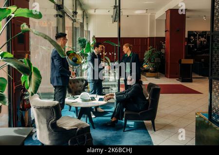 Eine reife Geschäftsfrau, die in der Hotellounge mit einem Geschäftsmann von männlichen und weiblichen Kollegen Handschlag machte Stockfoto