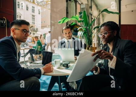 Junge Geschäftsfrau diskutiert über Dokument mit männlichen Kollegen sitzen in der Hotel Lounge Stockfoto