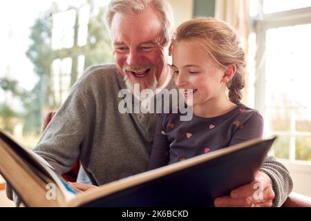Großvater Und Enkelin Schauen Sich Gemeinsam Das Fotoalbum In Der Lounge Zu Hause An Stockfoto