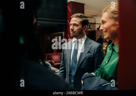 Lächelnde, reife Geschäftsfrau, die in der Hotellounge neben einem männlichen Profi steht Stockfoto