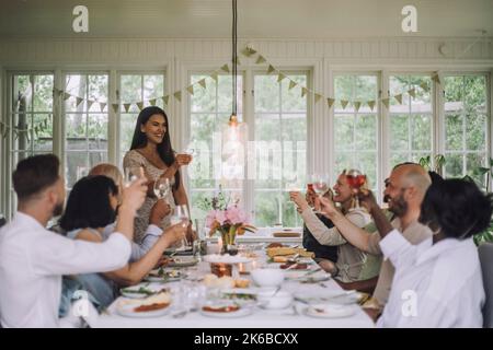 Lächelnde Frau, die während der Dinner-Party zu Hause einen Drink mit den Familienmitgliedern toasting Stockfoto