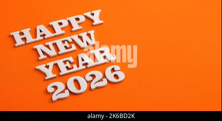 Frohes neues Jahr 2026 in Holzbuchstaben auf orangefarbenem Hintergrund Stockfoto