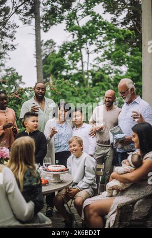 Junge sitzt auf einem Stuhl inmitten glücklicher Familienmitglieder während der Geburtstagsfeier Stockfoto