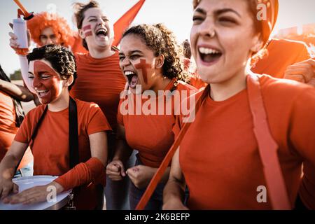 Fußballfans jubelten beim Fußballspiel im Stadion - Frauen mit gemaltem Gesicht und Trommel ermutigen ihr Team - Sport-Entertainment-Konzept Stockfoto