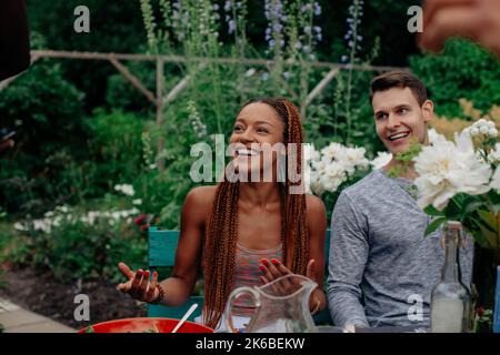 Glückliche Frau mit geflochtenen Haaren gestikulierte beim Reden auf Gartenparty Stockfoto